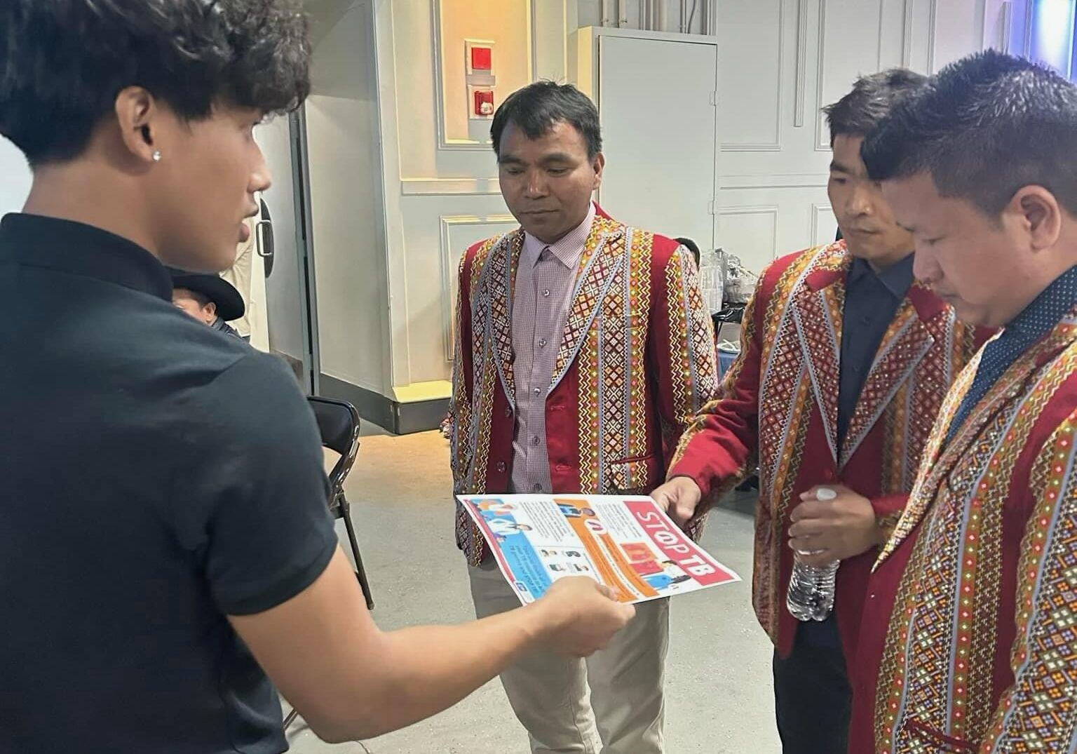 young man showing flyer to three men in red jackets looking to get involved