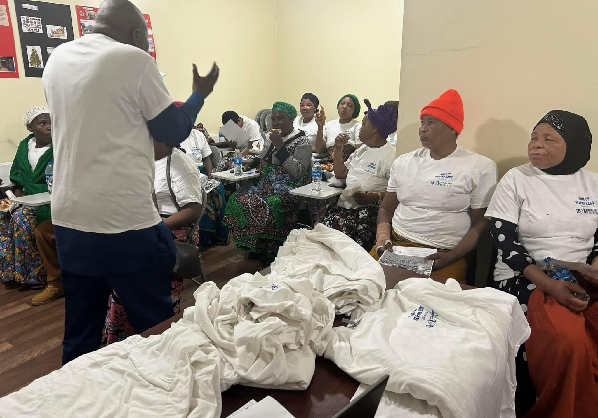 many people in classroom at desks wearing white shirts with Home of Helping Hand logo